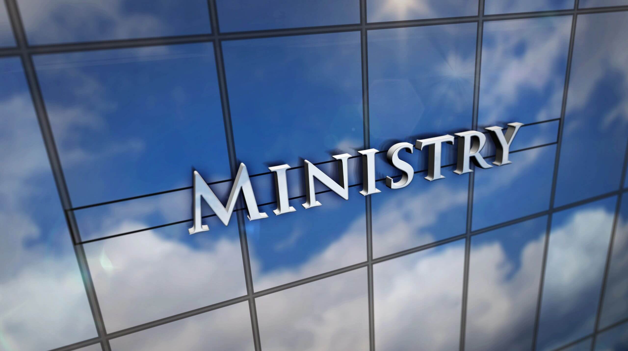Reflective glass building facade with the word 'MINISTRY' displayed.