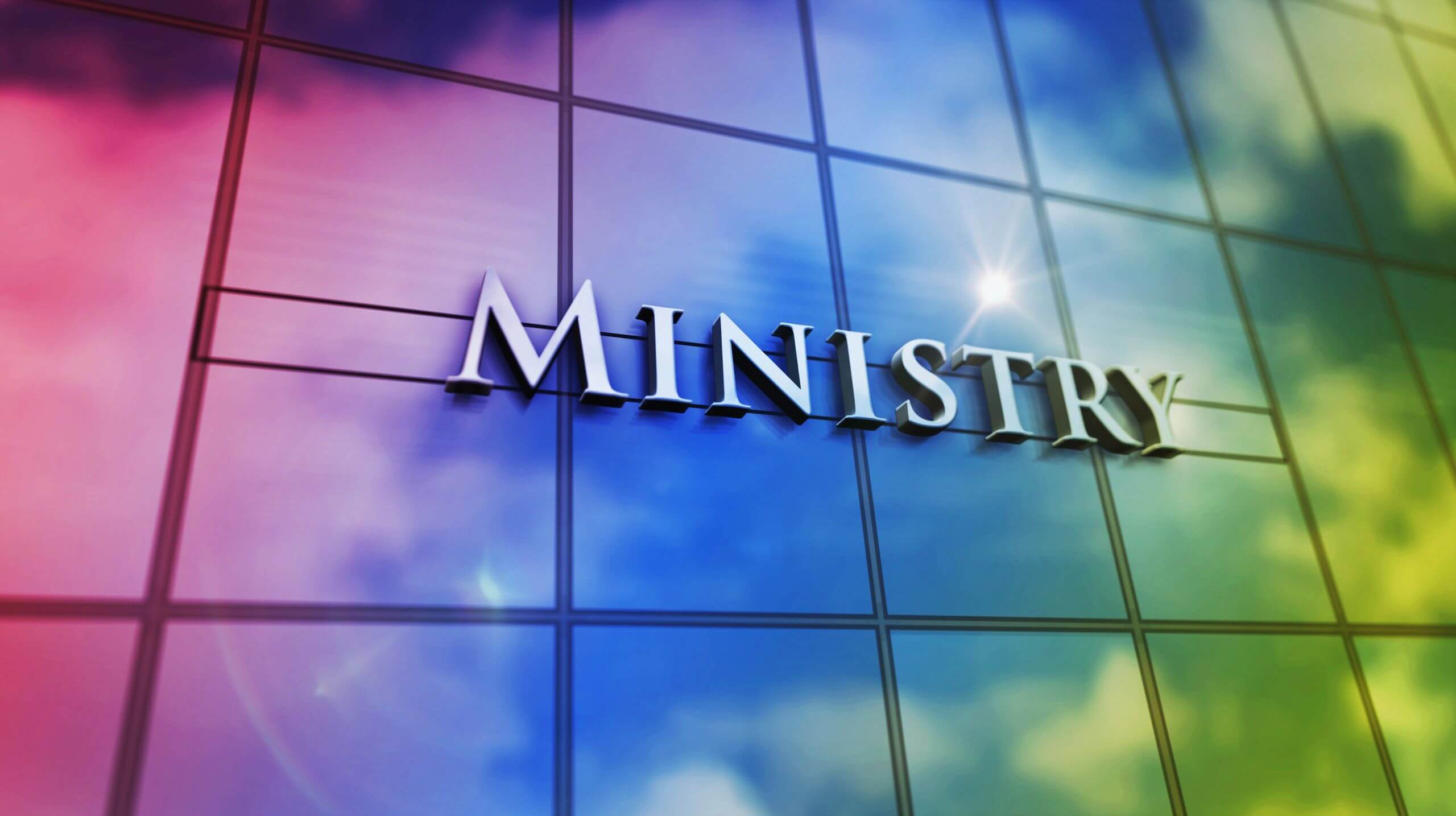 Close-up of the word 'MINISTRY' on a reflective glass building facade.