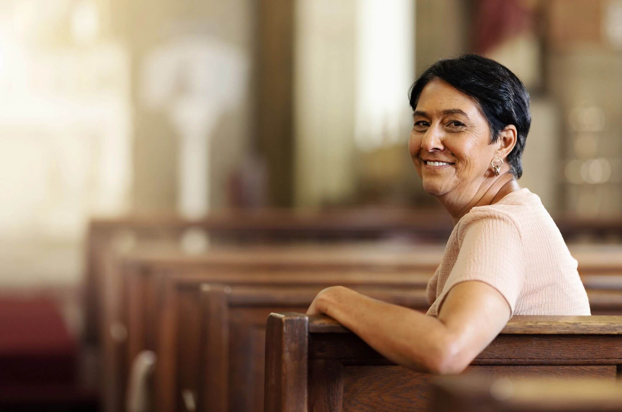 A woman smiling while sitting on a wooden pew in a church.