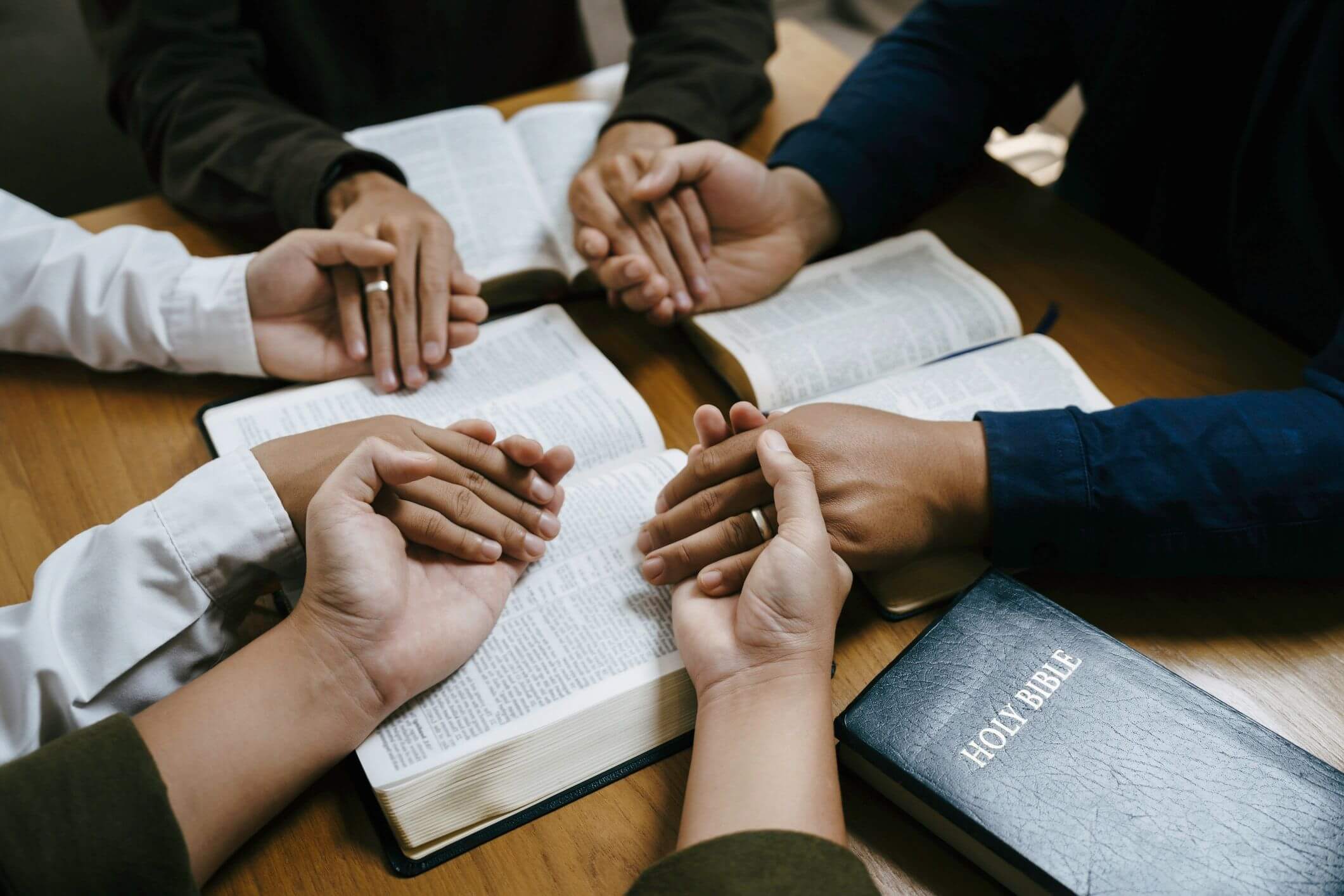 Group holding hands in prayer over open Bibles.