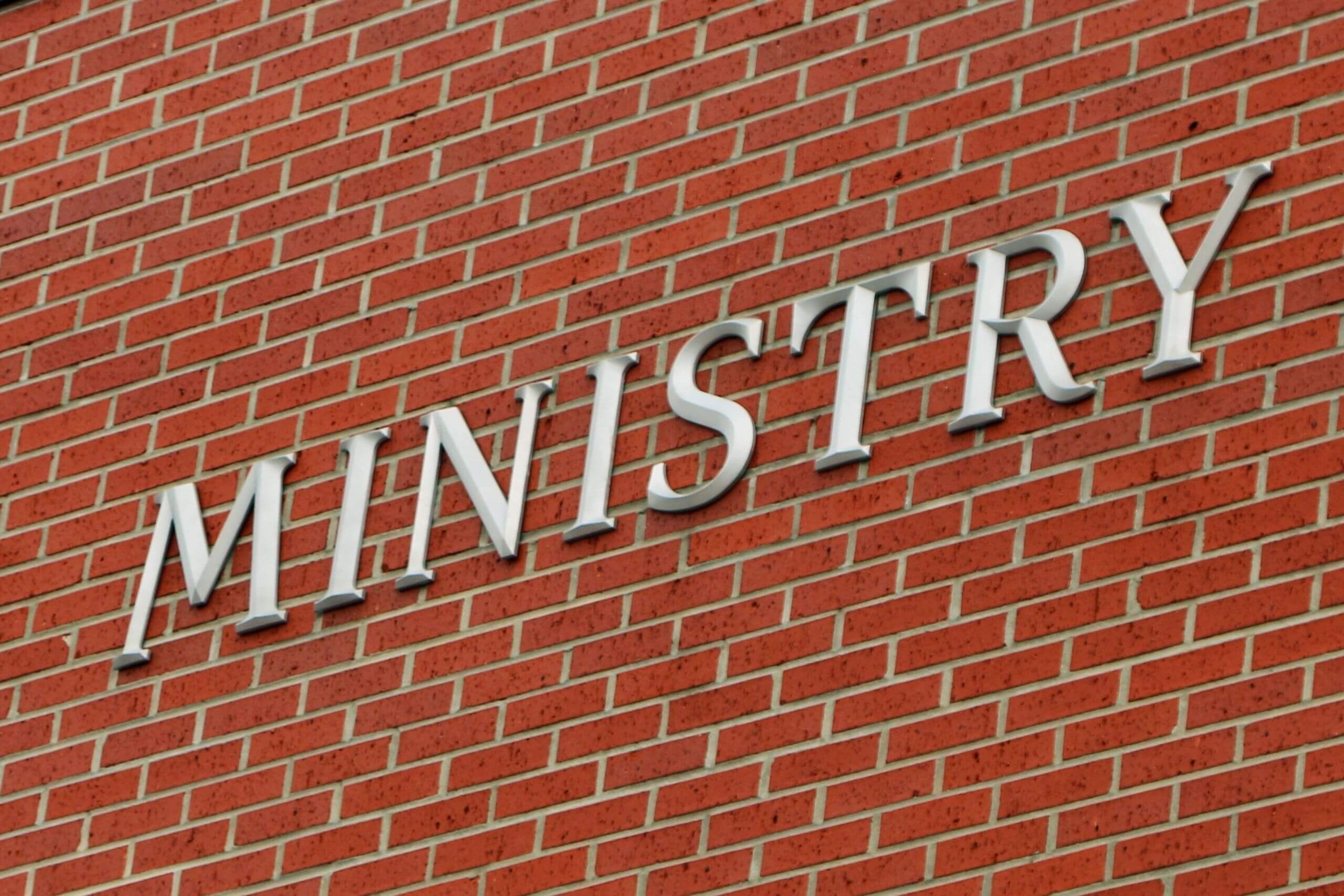 Partial view of a brick wall with the word 'MINISTRY' in metal letters.
